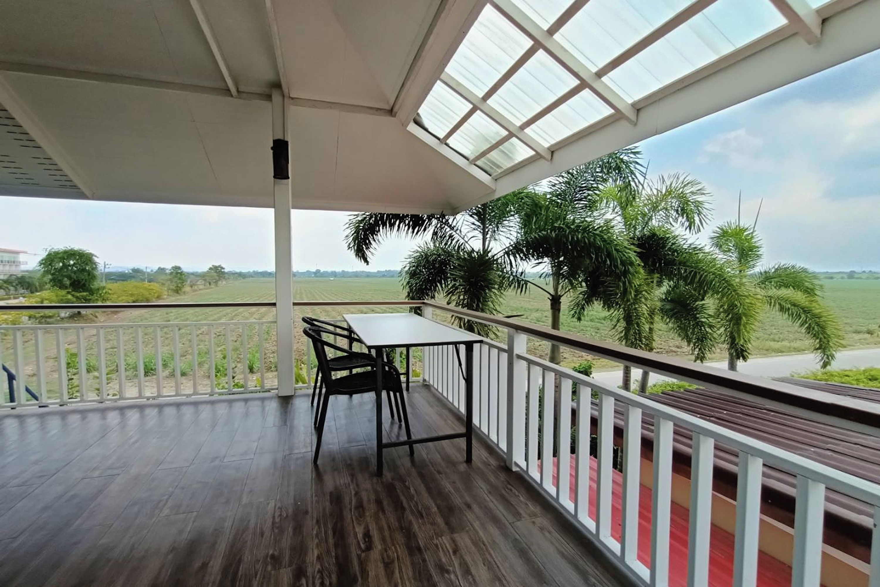 A covered balcony with a table and chairs, overlooking a green landscape with trees and a road.