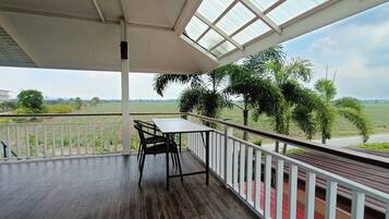 A covered balcony with a table and chairs, overlooking a green landscape with trees and a road.