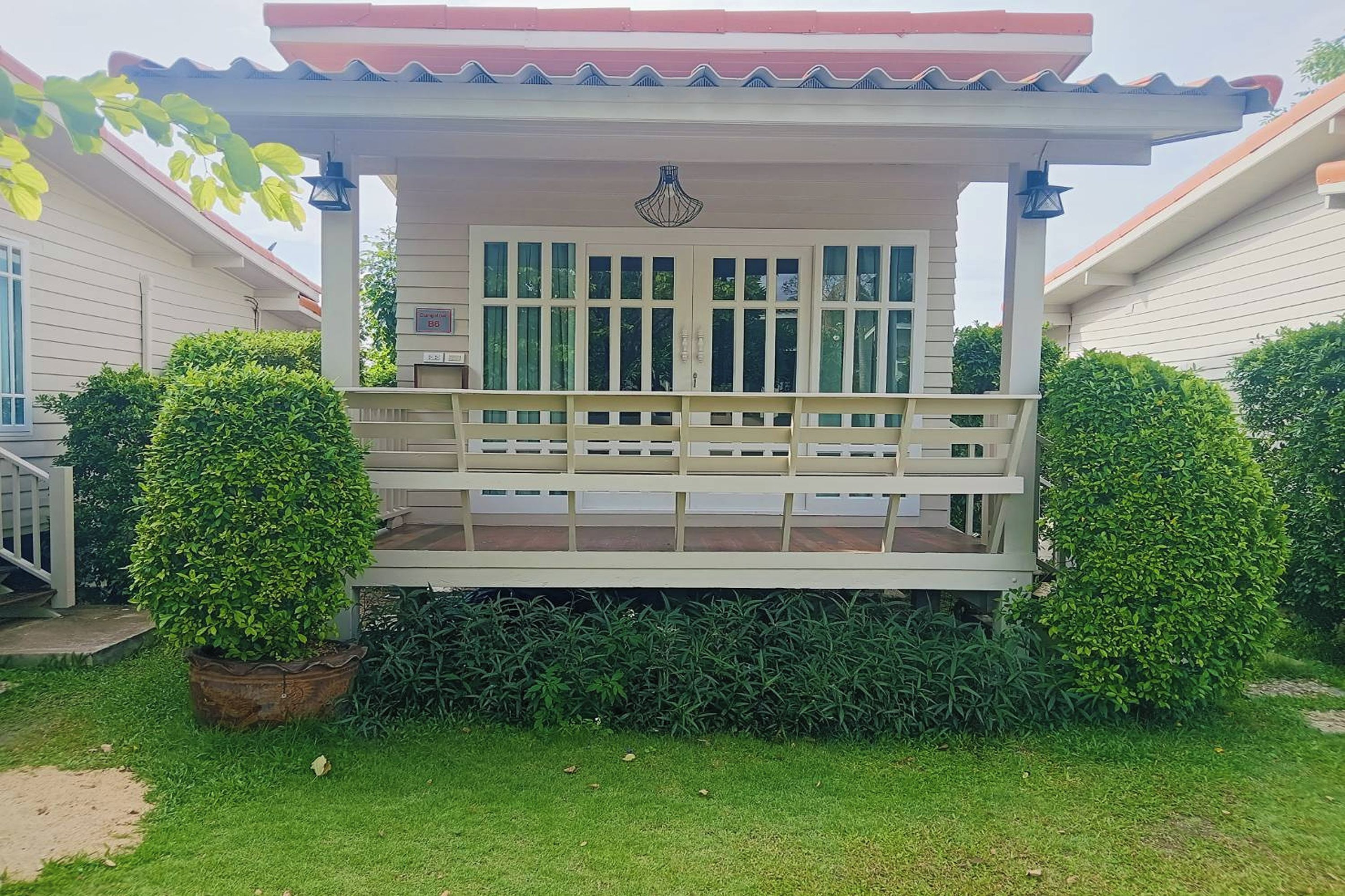 A covered porch with a bench, surrounded by well-maintained hedges and a potted plant.