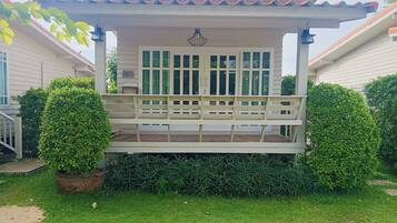 A covered porch with a bench, surrounded by well-maintained hedges and a potted plant.