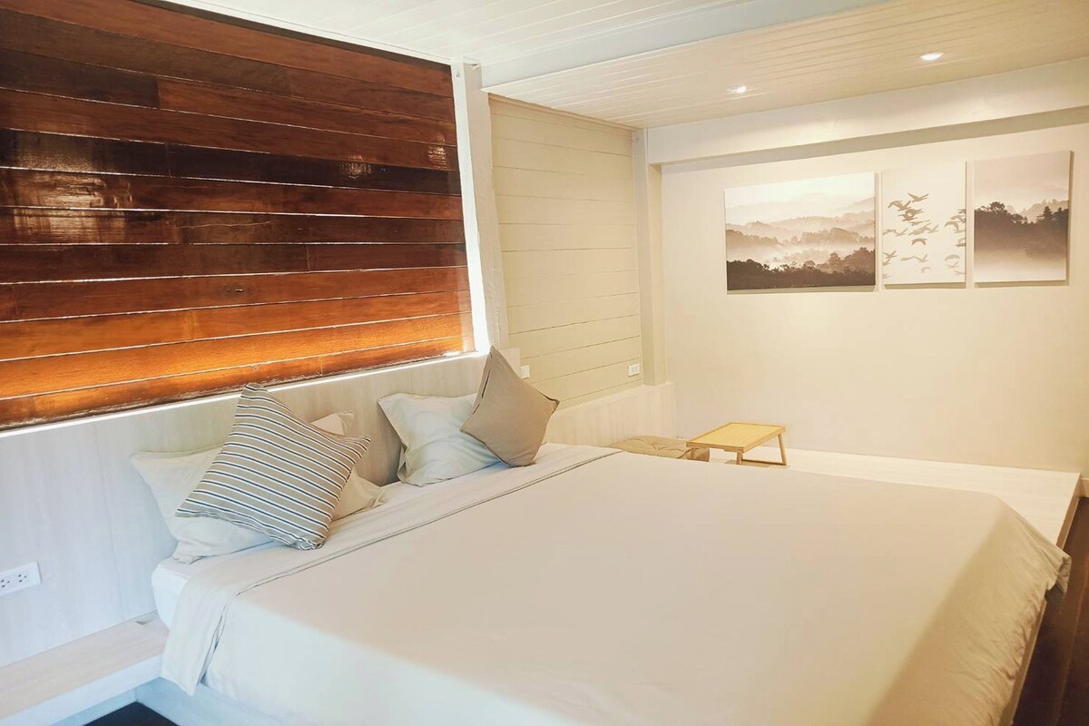 Un dormitorio con una cama grande, cabecera de madera, mesita de noche y cuadros en la pared.