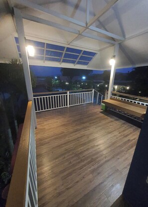Un espacio al aire libre techado con piso de madera y barandas blancas.