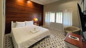 Habitación de hotel con una cama grande, un escritorio, una silla, un televisor y una ventana con cortinas.