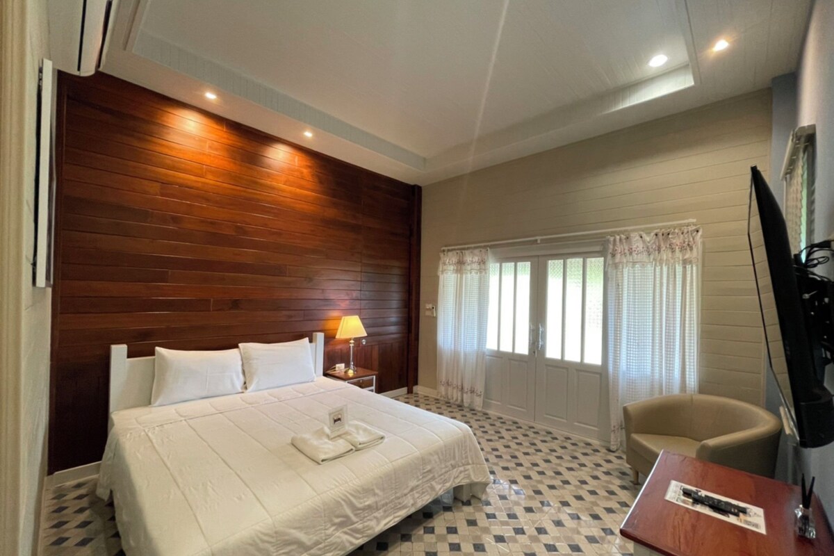 A hotel room with a large bed, a desk, a chair, a TV, and a window with curtains.