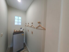 Un couloir étroit avec un réfrigérateur, des cintres en bois accrochés au mur et une fenêtre.