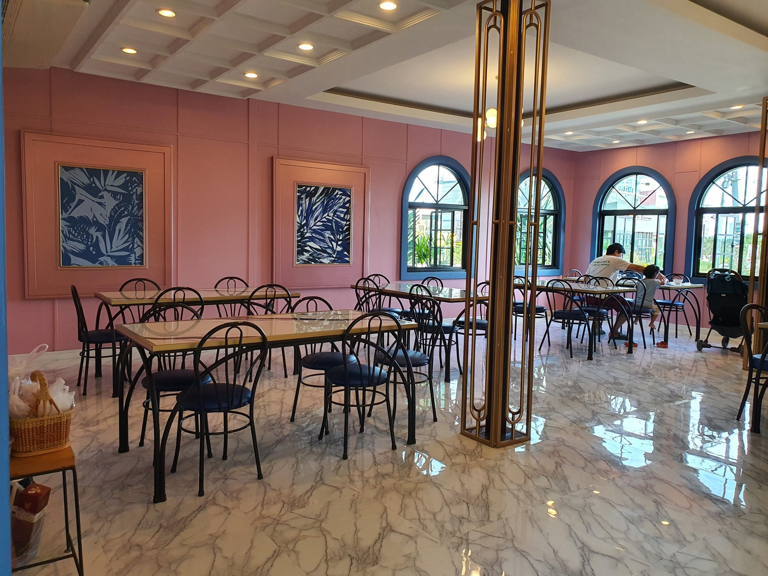 A spacious dining area with marble flooring, multiple tables and chairs, large windows, and artwork on the walls.