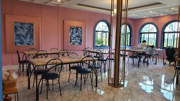 A spacious dining area with marble flooring, multiple tables and chairs, large windows, and artwork on the walls.