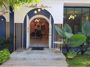 Una entrada de edificio con un letrero que dice 'Aob - Un', un comedor con mesas y sillas, y plantas verdes grandes.