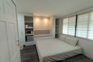 Un dormitorio con cama, estanterías empotradas, microondas y ventana con persianas.