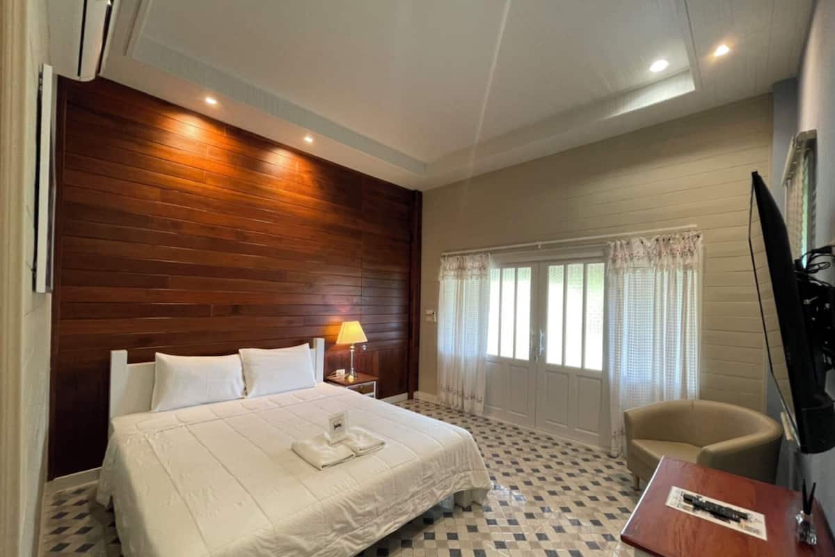 Habitación de hotel con una cama grande, un escritorio, una silla, un televisor y una ventana con cortinas.