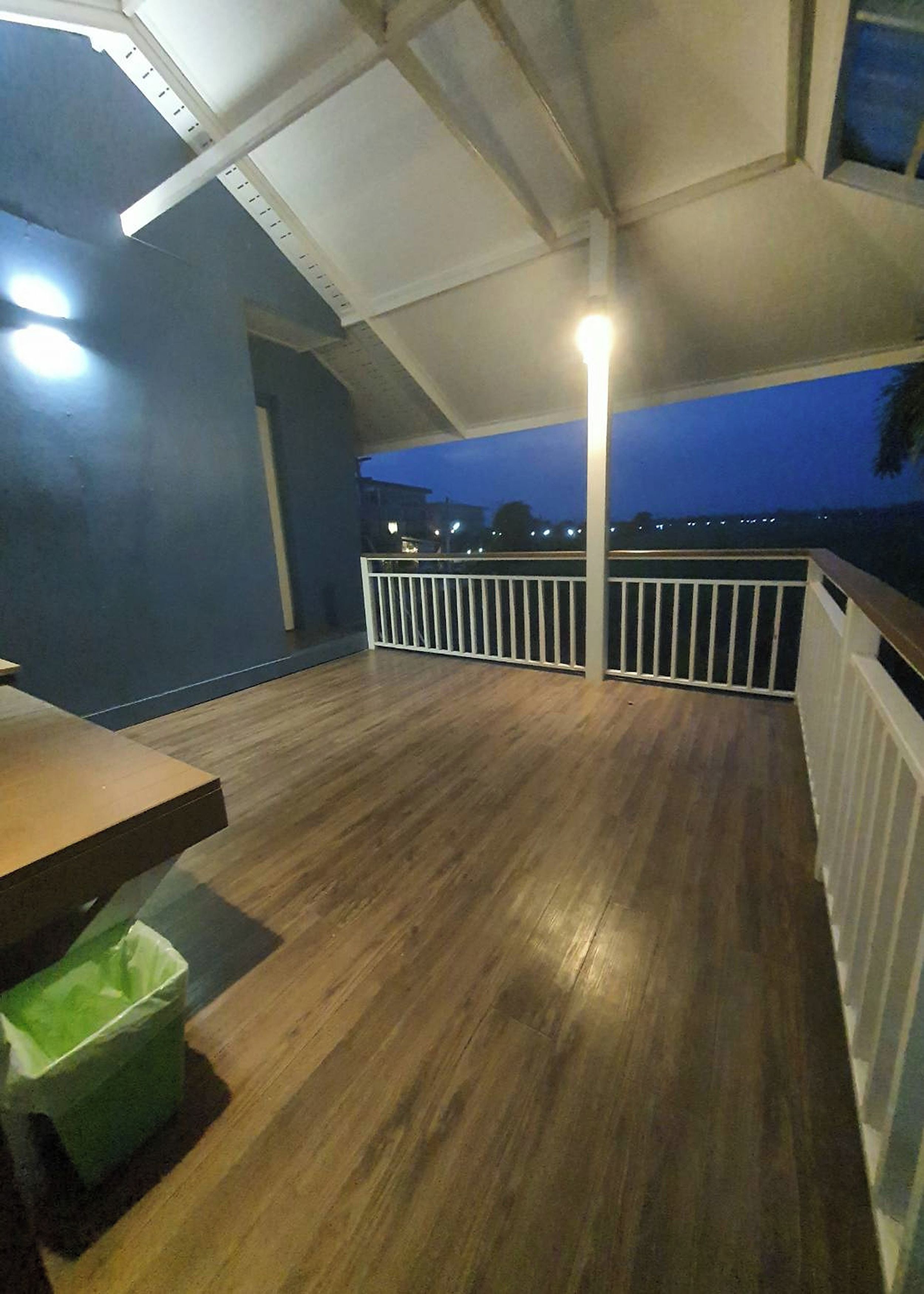 Varanda interna com piso de madeira, corrimão branco e vista da cidade ao entardecer.