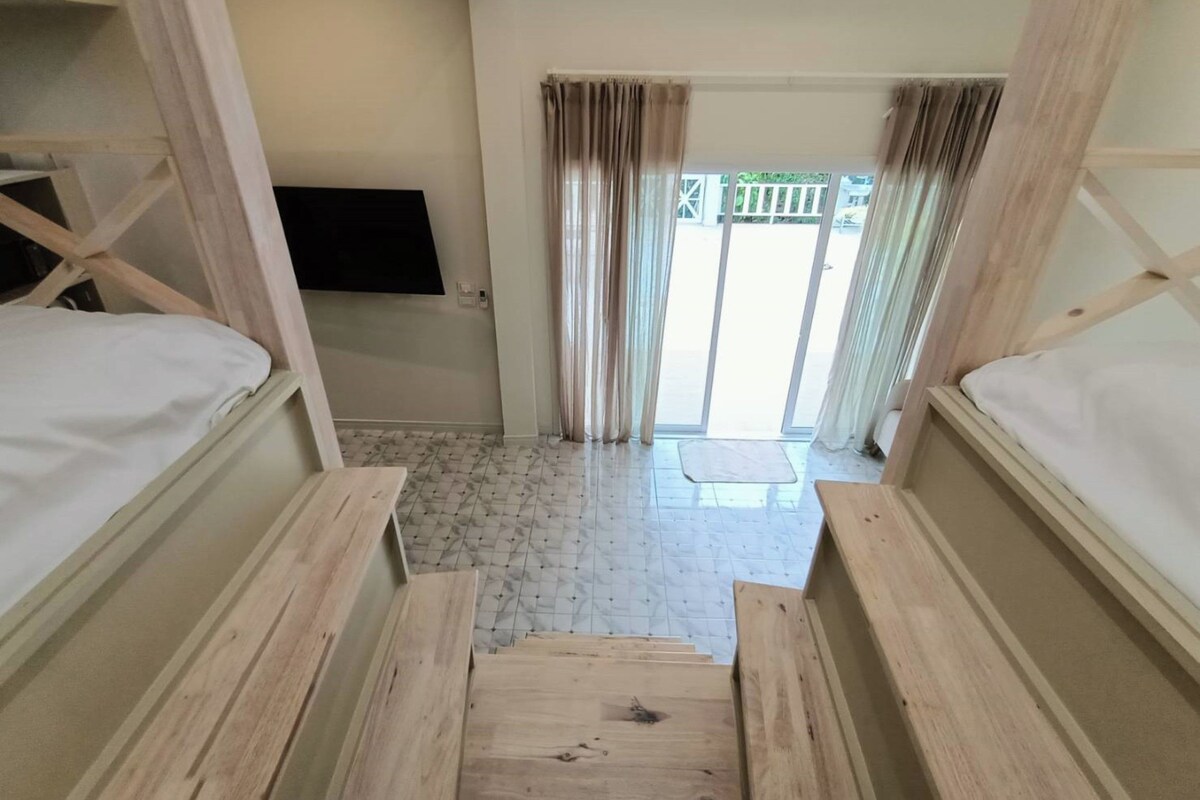 A room with bunk beds, a flat-screen TV, a sliding glass door leading outside, and a tiled floor.