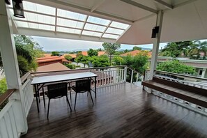 Un balcon abrité, doté d’une table et de chaises, d’un plancher en bois et offrant une vue sur les maisons et la verdure.