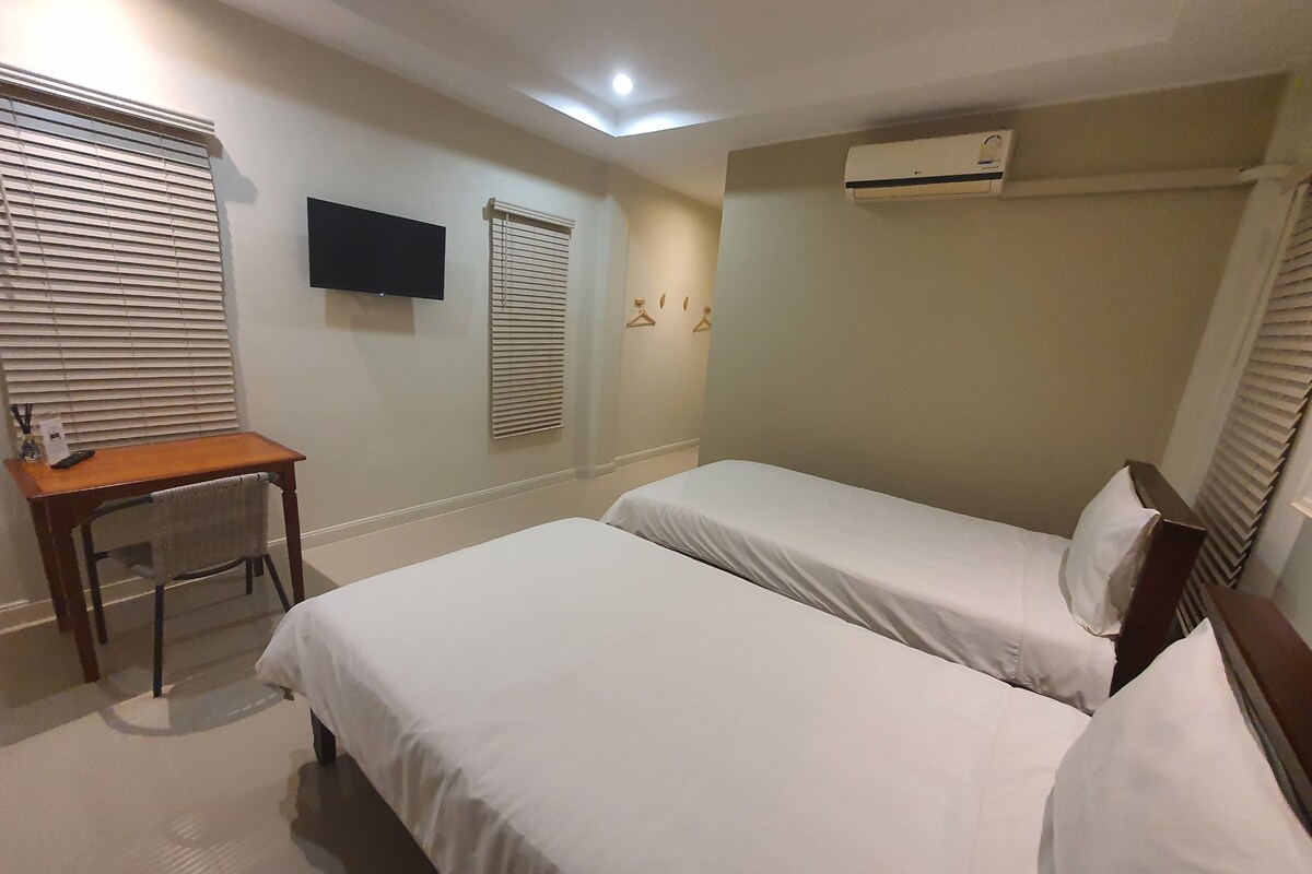 Habitación de hotel con dos camas individuales, un escritorio con silla, un televisor de pantalla plana en la pared y un equipo de aire acondicionado.
