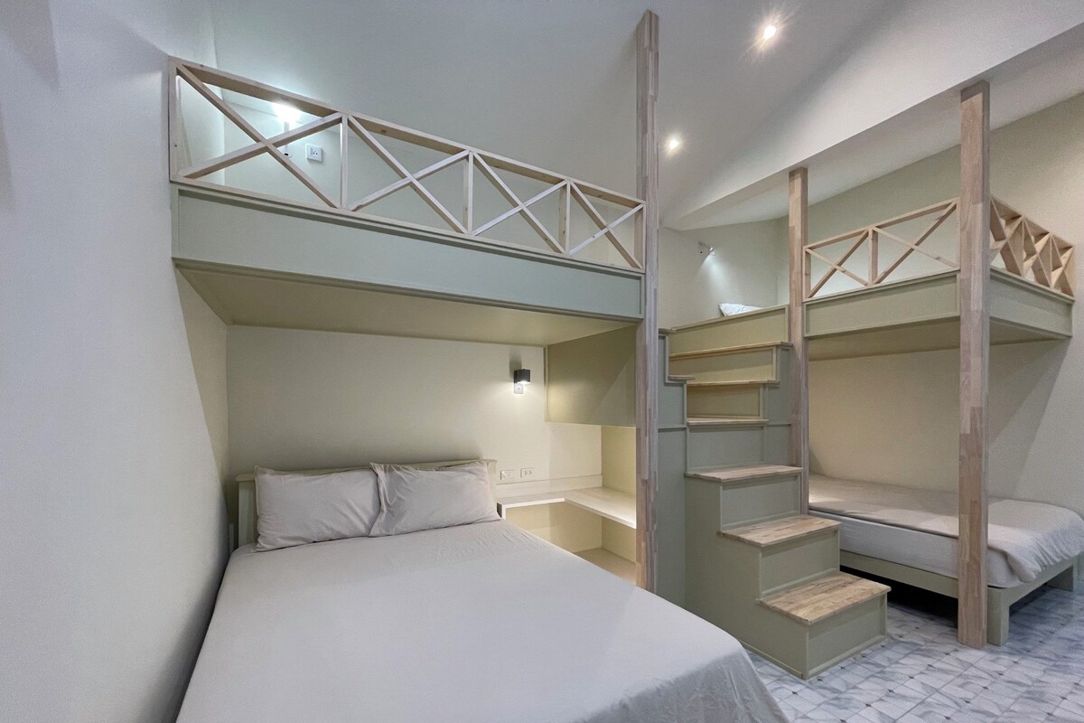 A room with bunk beds, a bedside table, and a wall-mounted light fixture.