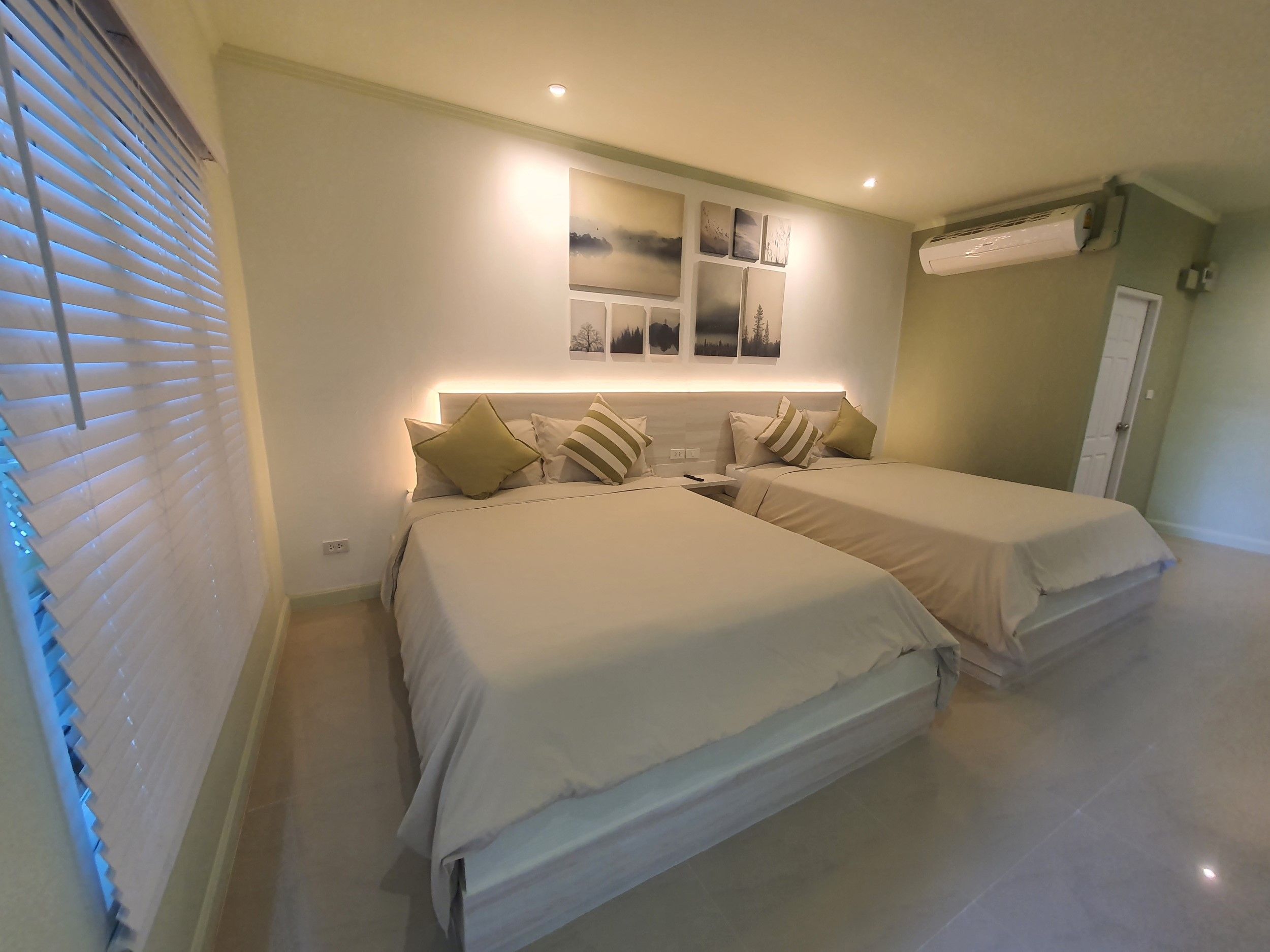 A hotel room with two beds, a wall-mounted air conditioner, and a window with blinds.
