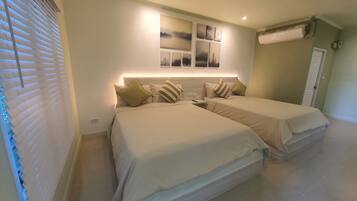 A hotel room with two beds, a wall-mounted air conditioner, and a window with blinds.