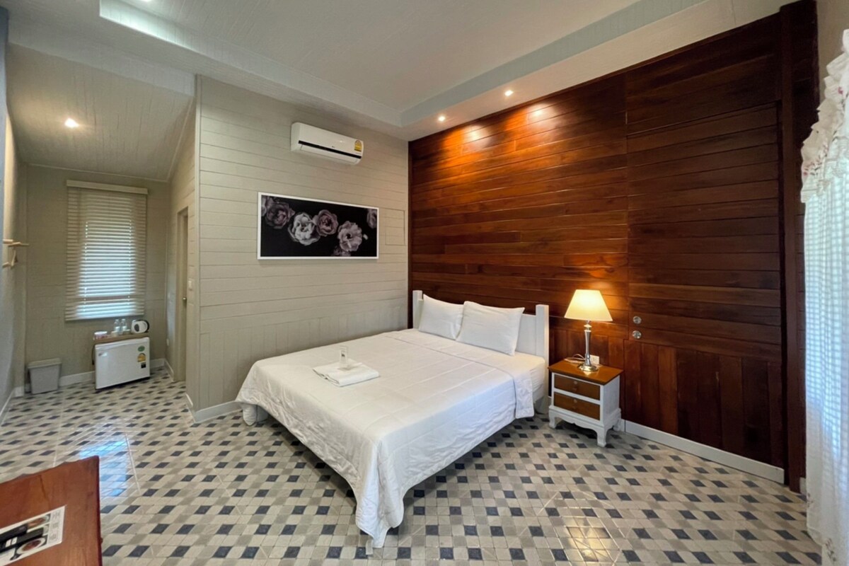 Un dormitorio con cama, mesita de noche, aire acondicionado instalado en la pared, ventana con persianas y suelo a cuadros.