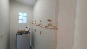 A narrow hallway with a refrigerator, wooden hangers on the wall, and a window with blinds.