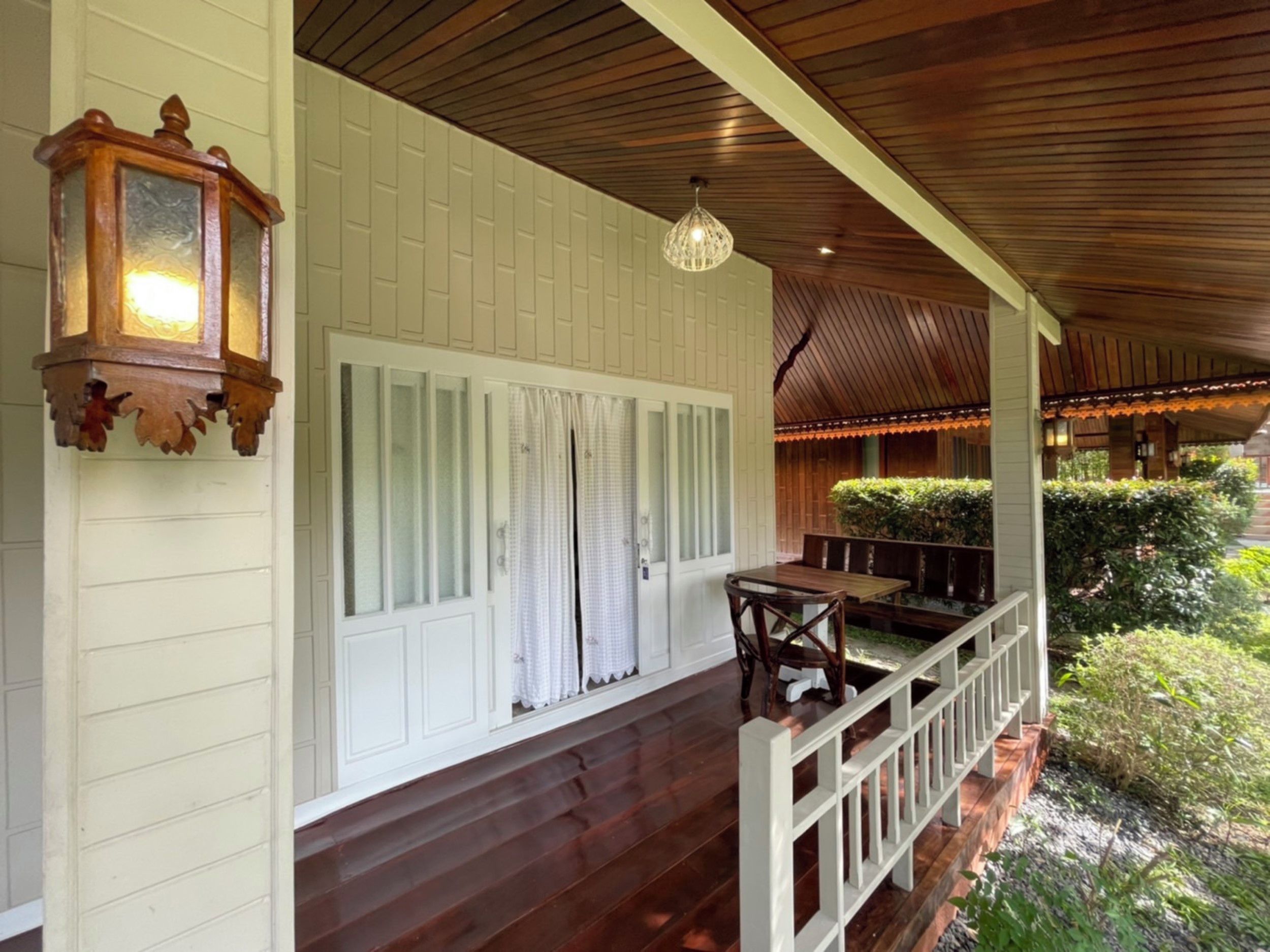 A covered porch with a wooden ceiling, white paneled walls, a wooden table and chairs, and a hanging light fixture.