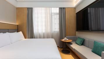 A modern hotel room with a large bed, a sofa, a small table, and a TV.