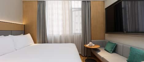 Una habitación de hotel moderna con una cama grande, un sofá, una mesita y un televisor.