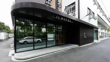 A modern hotel entrance with a glass facade, a car parked outside, and a clear view of the street.