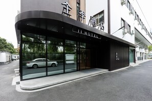 Una entrada de hotel moderna con fachada de vidrio, un automóvil estacionado afuera y una vista despejada de la calle.