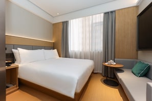 Ein modernes Hotelzimmer mit einem großen Bett, einer Couch, einem kleinen Tisch und einem Fernseher.