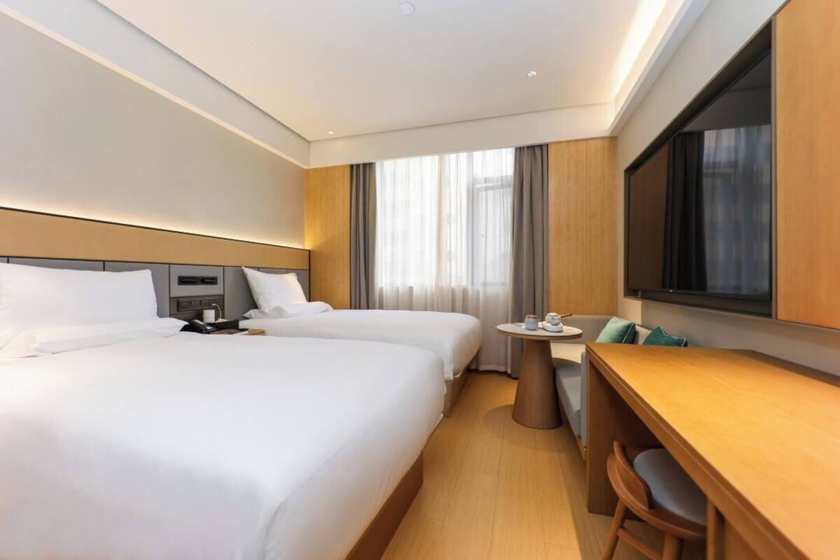 Quarto de hotel com duas camas, uma escrivaninha, uma cadeira, uma mesa redonda pequena e uma televisão.