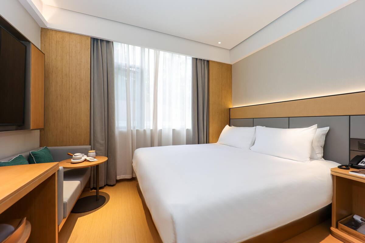Quarto de hotel com cama, escrivaninha, cadeira, televisão e janela com cortinas.