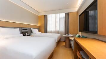 A hotel room with two beds, a desk, a chair, a TV, and a window with curtains.