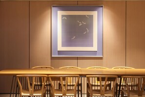 Une salle de conférence avec une longue table et des chaises, une œuvre d’art encadrée au mur et un lambris en bois.
