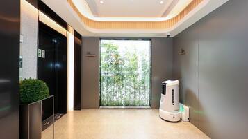 A modern elevator with a digital display, a potted plant, and a robotic vacuum cleaner in a clean, well-lit lobby area.