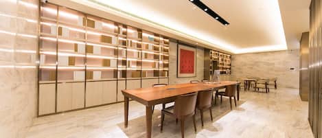 A modern interior with a long wooden table, multiple chairs, and built-in bookshelves.