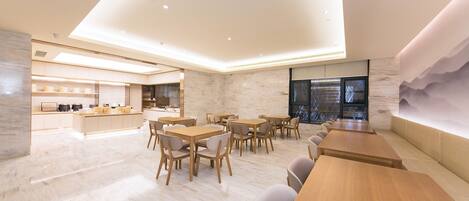 Un espace repas moderne avec des tables et des chaises en bois, une cuisine en arrière-plan et une grande fenêtre offrant une belle vue.