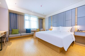 Ein modernes Hotelzimmer mit einem großen Bett, einem Schreibtisch und einer Sitzecke mit einer Couch und einem Sessel.