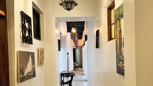 A hallway with a patterned floor, decorative wall art, and a hanging light fixture. - Emerald Palm Courtyard Hotel (Zanzibar Town)