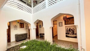 An interior courtyard with a white lattice ceiling, a central grassy area, and a staircase leading to an upper level. - Emerald Palm Courtyard Hotel (Zanzibar Town)