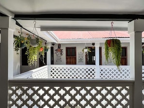 A covered porch with hanging plants, a white lattice railing, and a red-tiled roof. - Emerald Palm Courtyard Hotel (Zanzibar Town)