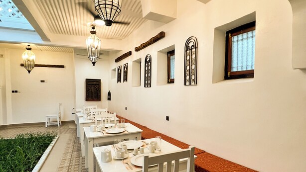 A dining area with white tables and chairs, decorative wall sconces, and a patterned floor. - Emerald Palm Courtyard Hotel (Zanzibar Town)