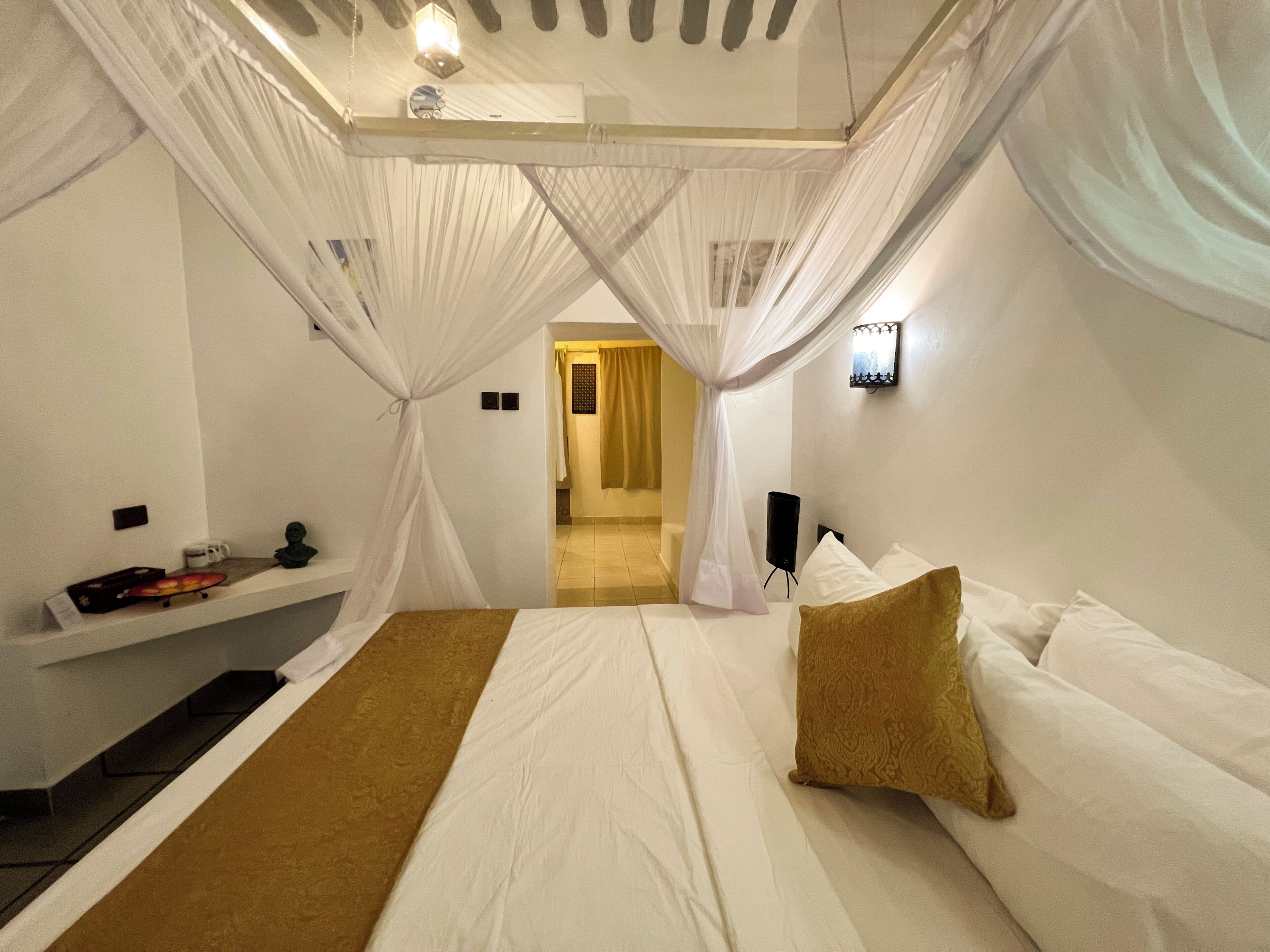 Een slaapkamer met een bed, een nachtkastje, een speaker aan de muur en een deur naar een andere kamer.