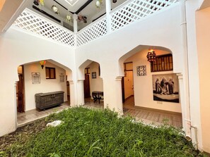An interior courtyard with a white lattice ceiling, a central grassy area, and a staircase leading to an upper level. - Emerald Palm Courtyard Hotel (Zanzibar Town)