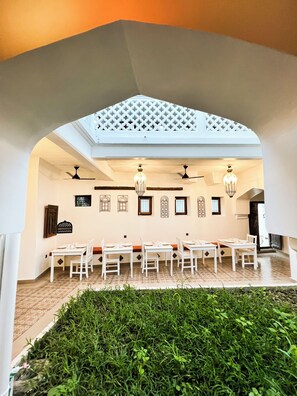 Un comedor con mesas y sillas blancas, un ventilador de techo y decoración en las paredes.