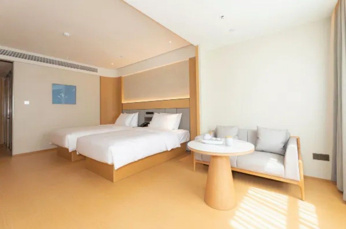 A modern hotel room with a large bed, a sofa, a round table, and a view of the city.