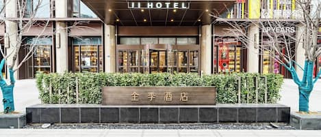 L’entrée d’un hôtel, avec une enseigne indiquant « JI HOTEL » et une plaque nominative devant.