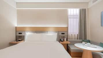 Quarto de hotel com uma cama grande, mesas de cabeceira, uma mesa redonda e um espaço de estar.