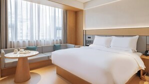 Habitación de hotel con una cama grande, un sofá cama, una mesita de noche y una ventana con cortinas.