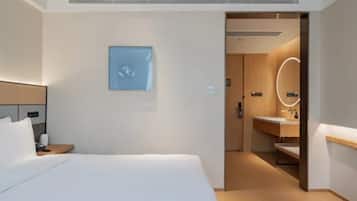 A hotel room with a bed, a bedside table, a wall-mounted picture, and a bathroom visible through an open door.