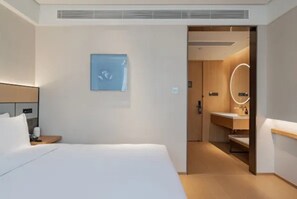 A hotel room with a bed, a bedside table, a wall-mounted picture, and a bathroom visible through an open door. - Ji Hotel (Tianjin)